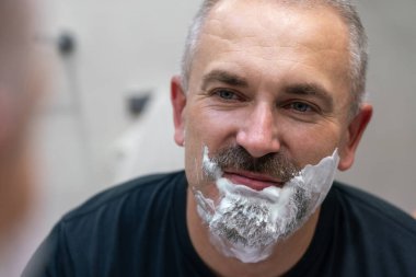 Orta yaşlı yakışıklı adam banyoda sakalını kesiyor.