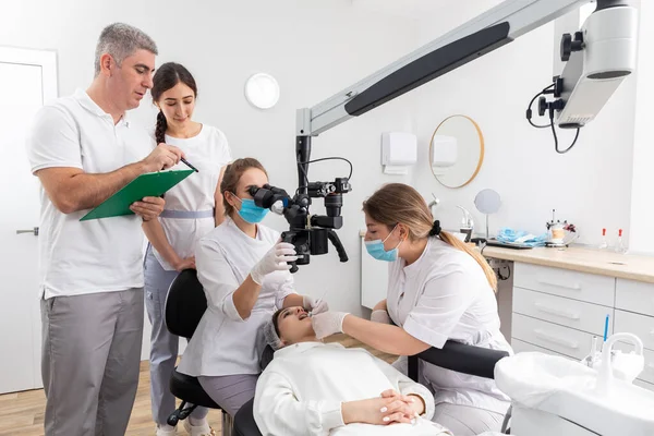 Group of students in dental clinic learn watching dental treatment with microscope