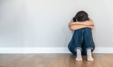 Üzgün kadın boş bir odada yerde yalnız başına, umutsuzluk ve yalnızlık içinde.
