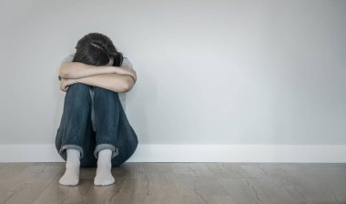 Üzgün kadın boş bir odada yerde yalnız başına, umutsuzluk ve yalnızlık içinde.