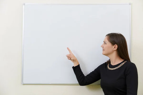 Young teacher sitting at a table near empty white board in a classroom