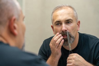 Middle-aged handsome man using scissors to cut his beard a litlie 