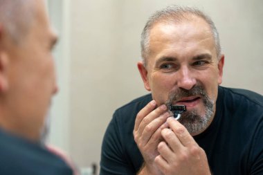 Middle-aged handsome man using razor in a bathroom