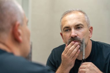 Middle-aged handsome man using scissors to cut his beard a litlie 