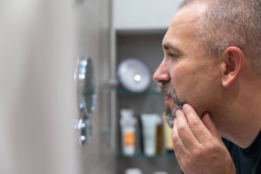 Middle-aged handsome man using razor in a bathroom