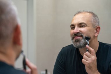Middle-aged handsome man using razor in a bathroom