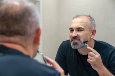 Middle-aged handsome man using razor in a bathroom