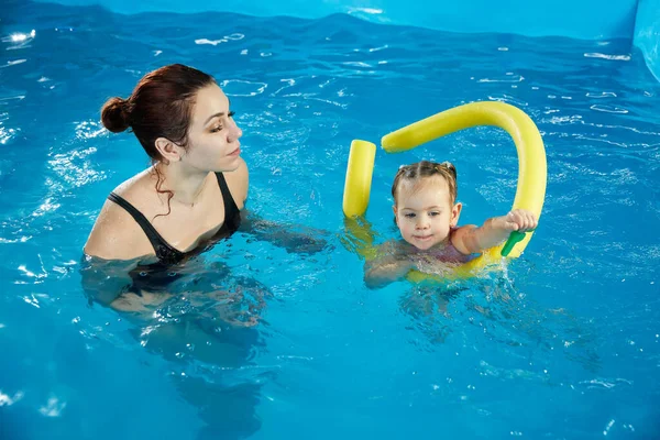 Preschool girl learning to swim in a pool with noodle