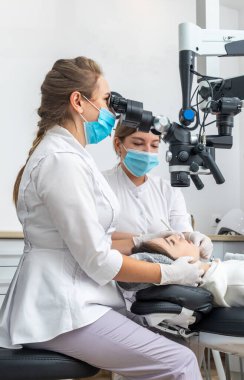 Female dentist using dental microscope treating patient teeth at dental clinic office. Medicine, dentistry and health care concept