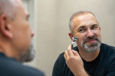 Middle-aged handsome man using razor in a bathroom