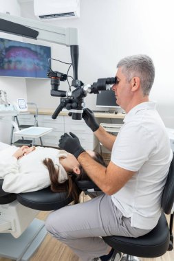 Dentist using dental microscope treating patient teeth at dental clinic office. Medicine, dentistry and health care concept