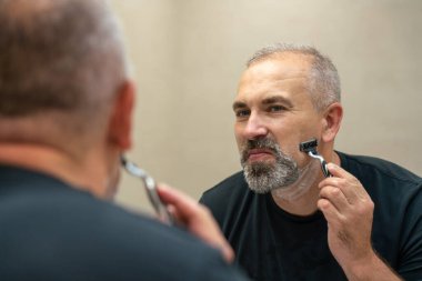 Middle-aged handsome man using razor in a bathroom