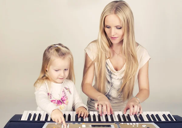 Kleines süßes Mädchen mit ihrer Mutter, die auf einem Synthesizer spielt — Stockfoto