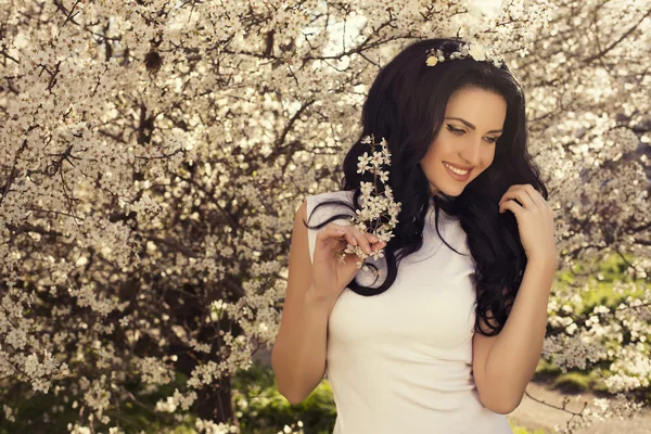 Vackra leende kvinna poserar på våren blomma trädgård — Stockfoto