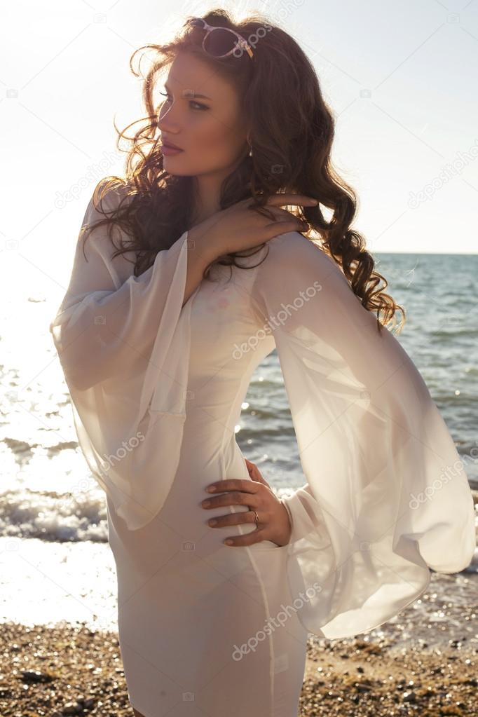 Beautiful girl in white dress posing on the beach in sunlight rays