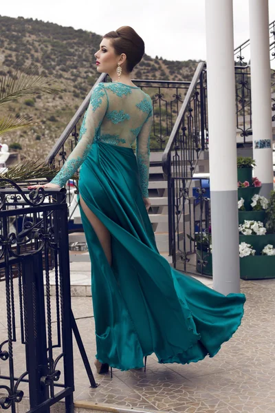 Zdjęcie moda model piękny seksowny z elegancką fryzurę w luksusowy jedwabny niebieski strój, pozowanie w stacji dokującej — Zdjęcie stockowe