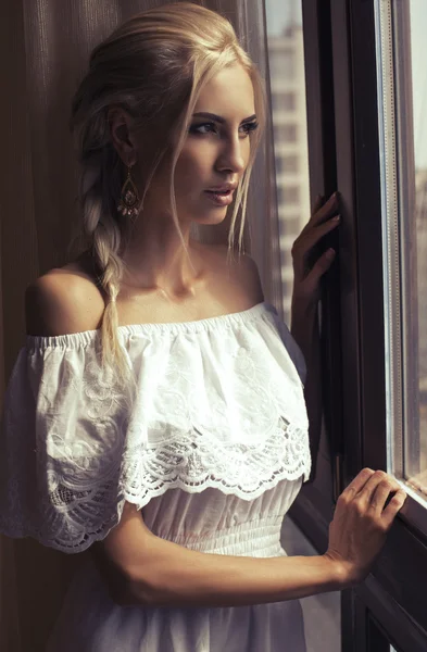 Mooie vrouw met blond haar dromen naast een venster — Stockfoto