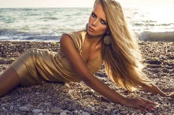 Сексуальна дівчина з світлим волоссям у золотій сукні позує на пляжі — стокове фото