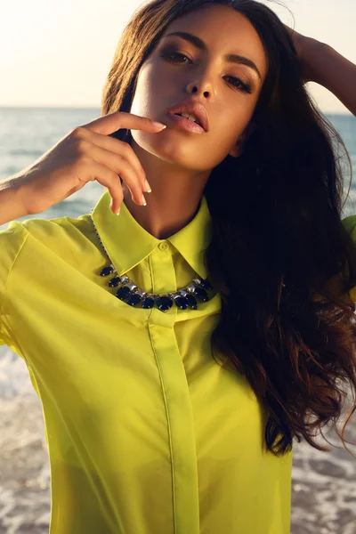 Porträtt av sexiga flicka med mörkt hår i ljusa skjorta poserar på stranden — Stockfoto