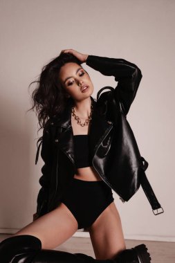 Siyah deri ceketli ve stüdyoda poz veren siyah saçlı güzel bir kadının moda fotoğrafı.