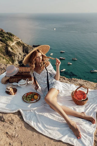 时尚户外照片 美丽的女人 金发碧眼 穿着雅致的衣服 在有海景的山上野餐 — 图库照片