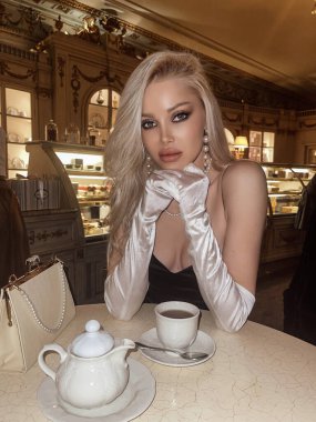 Şık elbiseli, sarı saçlı, lüks bir otelin kafesinde poz veren güzel bir kadının moda fotoğrafı. 