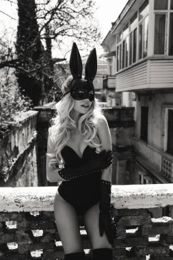 Güzel, siyah saçlı, zarif deri elbiseli ve tavşan maskeli bir kadının moda fotoğrafı.
