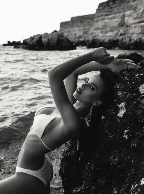 Gün batımı kumsalında poz veren siyah saçlı, şık yüzme takımlı güzel bir kadının moda fotoğrafı.