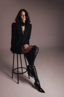 Güzel, siyah saçlı, zarif siyah iç çamaşırlı ve ceketli bir kadının stüdyoda poz verdiği bir moda fotoğrafı.