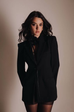 Güzel, siyah saçlı, zarif siyah iç çamaşırlı ve ceketli bir kadının stüdyoda poz verdiği bir moda fotoğrafı.