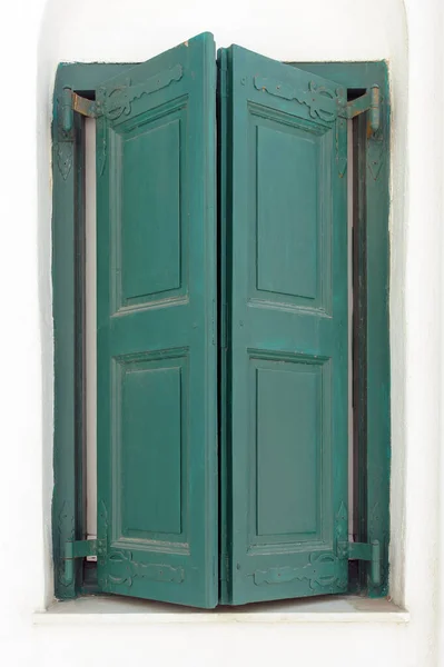 Window with green closed shutters on whitewashed wall