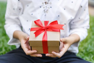 Female hands holding a gift wrapped with red ribbon