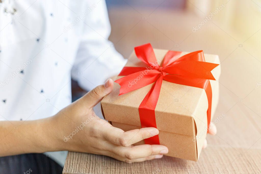Female hands holding a gift wrapped with red ribbon
