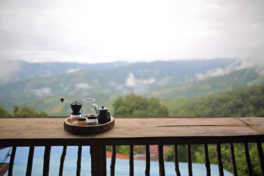 Kettle 'dan damlayan kahve poşeti doğadaki ahşap masa arkasında, sabah kahve saati dağ manzaralı ve doğal yeşil manzaralı soğuk ve rahat..