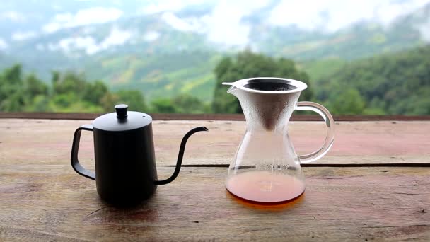 在大自然的背景下 玻璃杯 水壶里的咖啡滴落在木制桌子上 早上的咖啡时间 带着山景和自然绿景 感觉寒冷和放松 — 图库视频影像