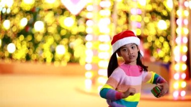 Yeni yıl beklentisi. Kırmızı bir Noel şapkası ve güzel bir renk tişörtü giyen ve arka planda Bokeh ışıkları olan tatlı küçük kız. Bu önemli sezonda iyi eğlenceler ve iyi eğlenceler..