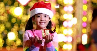 Yeni yıl beklentisi. Kırmızı bir Noel şapkası ve güzel bir renk tişörtü giyen ve arka planda Bokeh ışıkları olan tatlı küçük kız. Bu önemli sezonda iyi eğlenceler ve iyi eğlenceler..