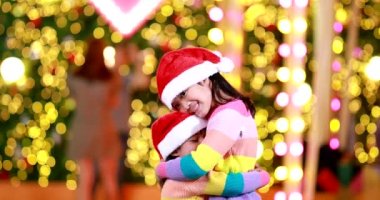 Yeni yıl beklentisi. Kırmızı bir Noel şapkası ve güzel bir renk tişörtü giyen iki tatlı kız. Arka planda Bokeh ışıkları var..