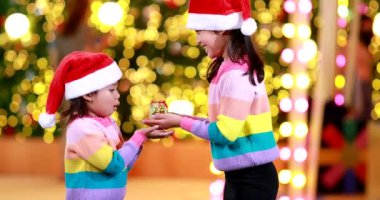 Yeni yıl beklentisi. Kırmızı bir Noel şapkası ve güzel bir renk tişörtü giyen iki tatlı kız. Arka planda Bokeh ışıkları var..