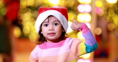 Yeni yıl beklentisi. Kırmızı bir Noel şapkası ve güzel bir renk tişörtü giyen ve arka planda Bokeh ışıkları olan tatlı küçük kız. Bu önemli sezonda iyi eğlenceler ve iyi eğlenceler..