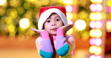 Yeni yıl beklentisi. Kırmızı bir Noel şapkası ve güzel bir renk tişörtü giyen ve arka planda Bokeh ışıkları olan tatlı küçük kız. Bu önemli sezonda iyi eğlenceler ve iyi eğlenceler..