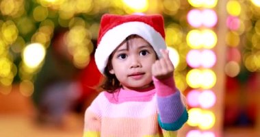 Yeni yıl beklentisi. Kırmızı bir Noel şapkası ve güzel bir renk tişörtü giyen ve arka planda Bokeh ışıkları olan tatlı küçük kız. Bu önemli sezonda iyi eğlenceler ve iyi eğlenceler..