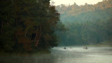 Pang Ung, Mae Hong Son, Tayland - 19 Aralık 2021: Sabahları ağaçlar ve doğa manzarasıyla gölün üzerinde yüzen bambu rafting yapan turist.