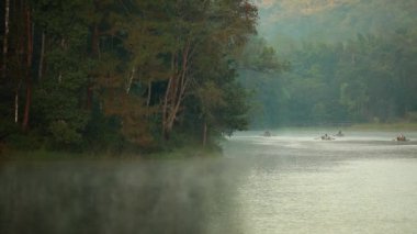 Pang Ung, Mae Hong Son, Tayland - 19 Aralık 2021: Sabahları ağaçlar ve doğa manzarasıyla gölün üzerinde yüzen bambu rafting yapan turist.