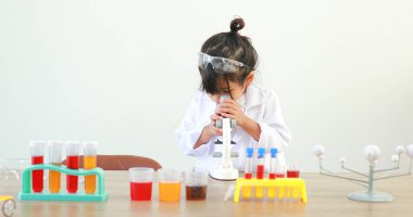 Küçük tatlı Asyalı öğrenci araştırma yapmayı ve kimyasal deney yapmayı öğrenirken evdeki test tüpünde sıvıyı analiz edip karıştırıyor..