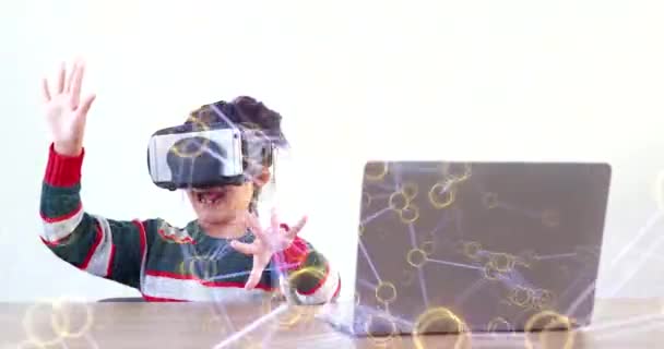 戴Vr的小女孩坐在桌子前 戴着家用眼镜 虚拟的全球互联网连接发生了变化 未来的孩子穿着白色衣服戴Vr耳机玩游戏 先进技术的概念 — 图库视频影像