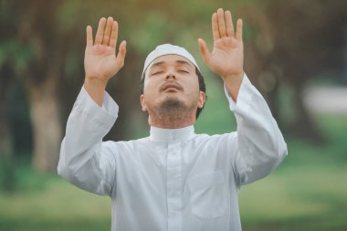 Religious muslim man  traditional kandura praying  outdoor at quiet nature  environment sun beams.