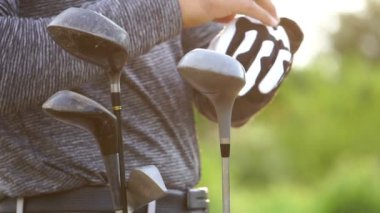 Golf çantasının yanında eldiven giyen adamın yakın plan görüntüsü.