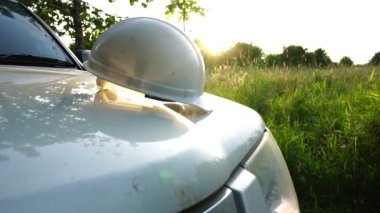 Kask takan ve tablet kullanan beyaz renkli bir arabanın yanında duran adam.