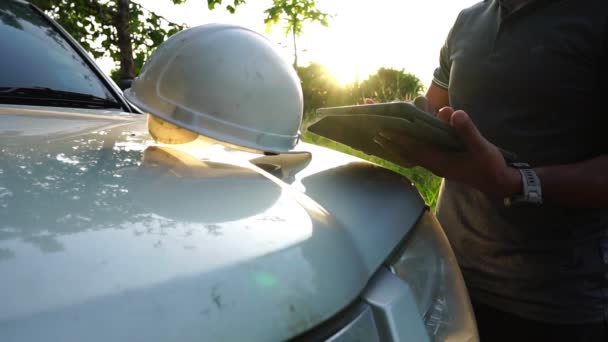 ヘルメットをかぶって白い色の車の近くに立ちタブレットを使って — ストック動画